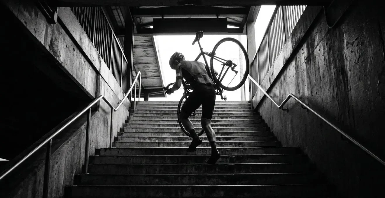 Cycliste portant son vélo sur l'épaule dans un escalier de gare